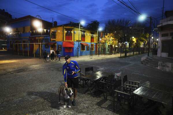 Boca Juniors fan Juan Gutierres, accompanied by his seven-year-old dog Rocco, stands outside watching a televised soccer match airing inside a restaurant, in La Boca neighborhood of Buenos Aires, Argentina, Sunday, May 4, 2025. (AP Photo/Natacha Pisarenko)