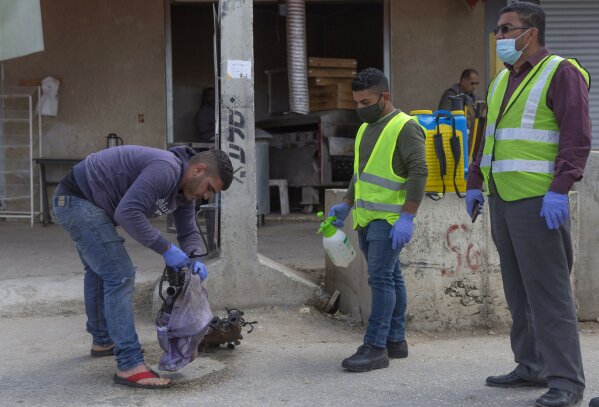 In this Tuesday, April 7, 2020 photo, a paramedic from the Palestinian Ministry of Health disinfects car parts carried by a Palestinian laborer, to help contain the coronavirus, as he exits an Israeli army checkpoint after returning from work in Israel, near the West Bank village of Nilin, west of Ramallah. The virus outbreak poses a major dilemma for tens of thousands of Palestinian laborers working inside Israel who can no longer freely travel back and forth. (AP Photo/Nasser Nasser)