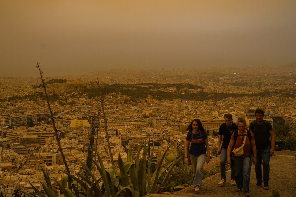Tourists walk at the Lycabettus hill as the city of Athens with the ancient Acropolis hill is seen at the background, on Tuesday, April 23, 2024. The Acropolis and other Athens landmarks took on Martian hues Tuesday as stifling dust clouds blown across the Mediterranean Sea from North Africa engulfed the Greek capital. (AP Photo/Petros Giannakouris)
