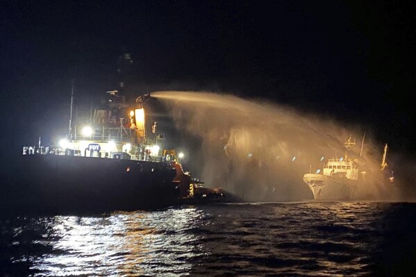 A firefighting-equipped tug boat, left, contacted by the Malta Vessel Traffic Services (VTS) helps controlling a fire occurred on the bow of the Conscience vessel in international waters of the Mediterranean Sea, Friday, May 2, 2025. (Malta Vessel Traffic Services via AP)