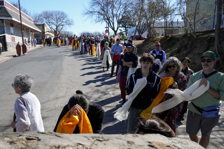 Buddhist faith leaders and community members drape Tibetan scarves on the Birthplace of Antioch marker during the "May We Gather" pilgrimage, Saturday, March 16, 2024, in Antioch, Calif. The event aimed to use karmic cleansing through chants, prayer and testimony to heal racial trauma caused by anti-Chinese discrimination in Antioch in the 1870s. (AP Photo/Godofredo A. Vasquez)