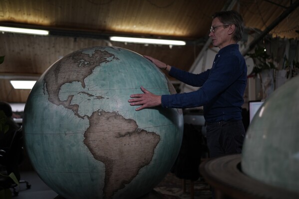 Peter Bellerby, the founder of Bellerby & Co. Globemakers, holds a globe at a studio in London, Tuesday, Feb. 27, 2024. Globes in the age of Google Earth capture the imagination and serve as snapshots of how the owners see the world and their place in it. Peter Bellerby made his first globe for his father, after he could not find one accurate or attractive enough. In 2008, he founded Bellerby & Co. Globemakers in London. His team of dozens of artists and cartographers has made thousands of bespoke globes up to 50 inches in diameter. The most ornate can cost six figures. (AP Photo/Kin Cheung)