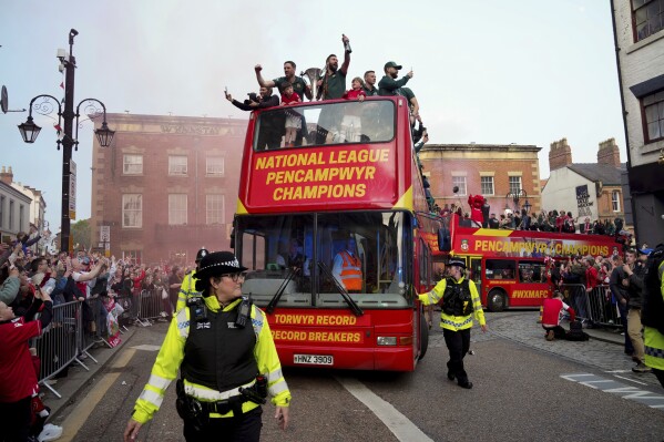 FILE - Members of the Wrexham FC soccer team ride on an open top bus as they celebrate promotion to the Football League in Wrexham, Wales, Tuesday, May 2, 2023. Wrexham was down on its luck and languishing in the fifth tier of English soccer before being given the A-list treatment by Reynolds and co-owner Rob McElhenney. Now it is embarking on a U.S. tour this month and fans of the globally-streamed docuseries “Welcome to Wrexham” will get to see its unlikely stars in the flesh. (AP Photo/Jon Super, file)