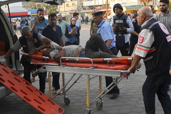 FILE - Journalists observe as a Palestinian man wounded in Israeli bombardment is brought to a hospital in Deir el-Balah, Gaza Strip, Monday, Oct. 16, 2023. Journalists reporting in Gaza need to worry about basic survival for themselves and their families in addition to getting out the story of a besieged population. (AP Photo/Adel Hana, File)