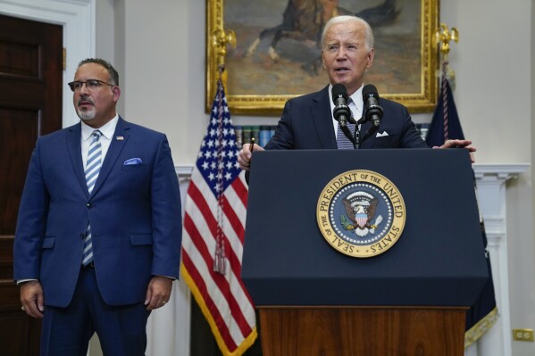 FILE - President Joe Biden speaks in the Roosevelt Room of the White House, June 30, 2023, in Washington, as his administration is moving forward on a new student debt relief plan after the Supreme Court struck down his original initiative. Education Secretary Miguel Cardona listens at left. Two conservative groups are asking a federal court to block the Biden administration’s plan to cancel $39 billion in student loans for more than 800,000 borrowers. (AP Photo/Evan Vucci, File)