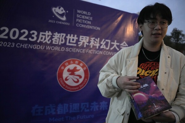 Tao Bolin, a 25-year-old influencer and science-fiction fan, holds a signed copy of "The Three-Body Problem" outside the World Science Fiction Convention in Chengdu, Sichuan province on Friday, Oct. 20, 2023. Tao grew up watching Japanese anime and always hoped his own country, China, would one day spawn science fiction stories enjoyed by the rest of the world. The series that began with "The Three-Body Problem," written by former engineer Liu Cixin, helped Chinese science fiction break through internationally, winning awards and making it onto the reading lists of the likes of former U.S. President Barack Obama and Mark Zuckerberg. (AP Photo/Ng Han Guan)