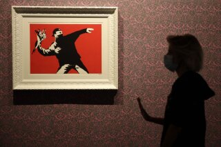 A worker walks past "Love Is in the Air", a screen print on paper, by British artist Banksy, a day before the unveiling of an exhibition in Rome, Monday, Sept. 7, 2020. The exhibition opens on Sept. 8 and runs until April 11, 2021. (AP Photo/Alessandra Tarantino)