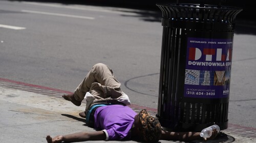 FILE - A homeless person lies on the sidewalk while holding a water bottle, Sunday, July 2, 2023, in downtown Los Angeles. Excessive heat warnings remain in place in many areas across the U.S. and are expected to last at least through Monday. (AP Photo/Damian Dovarganes, File)