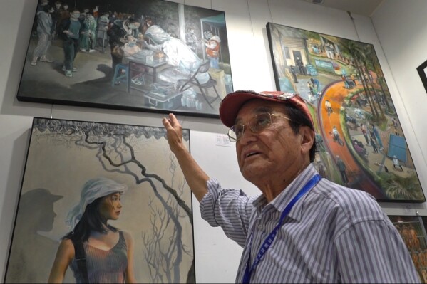 Zeng Fanzhi, a retired architect turned artist, points to his art work depicting a Covid testing scene, during the Beijing art exposition in Beijing, Friday, Sept. 8, 2023. Zeng painted stark, realist portrayals of life in China under zero-COVID, saying he did so to capture a unique moment in history. (AP Photo/Dake Kang)