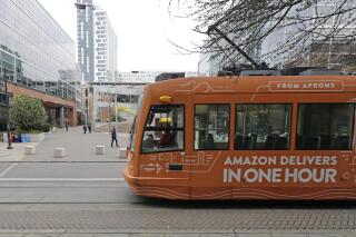 FILE - This Nov. 13, 2018 file photo a South Lake Union streetcar with an advertisement for Amazon.com's same-day delivery service passes by an Amazon office building in Seattle's South Lake Union neighborhood. Amazon has pushed back its return-to-office date for tech and corporate workers until January 2022 as COVID-19 cases surge nationally due to the delta variant. The Seattle Times reported on the tech giant's delay in returning to offices from internal messages. (AP Photo/Ted S. Warren,File)