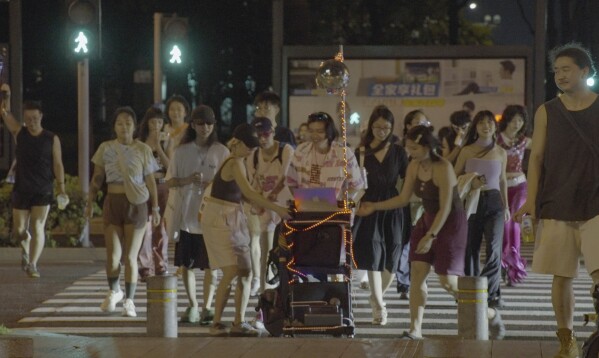 In this photo taken Sept. 8, 2023, attendees cross the road with DJ equipment on a cart during a public party organized by Loong Wu through streets of Shenzhen in southern China's Guangdong province. (Wu Peicheng via AP)