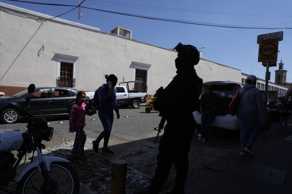 A municipal police officer stands guard in Maravatio, Michoacan state, Mexico, Tuesday, Feb. 27, 2024. Two mayoral hopefuls in this city were gunned down the previous day within hours of each other, ahead of the June 2 national elections. (AP Photo/Fernando Llano)