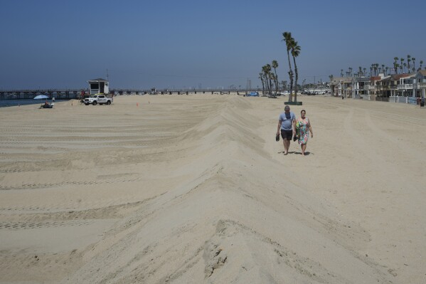 A couple walks along berms in Seal Beach, Calif., Friday, Aug. 18, 2023. Officials in Southern California were also re-enforcing sand berms, built to protect low-lying coastal communities against winter surf. Hurricane Hilary is churning off Mexico's Pacific coast as a powerful Category 4 storm threatening to unleash torrential rains on the mudslide-prone border city of Tijuana before heading into Southern California as the first tropical storm there in 84 years. (AP Photo/Damian Dovarganes)