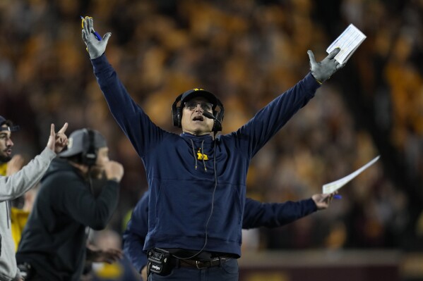 Michigan head coach Jim Harbaugh signals for a touchdown while looking at the replay board during the first half of an NCAA college football game against Minnesota, Saturday, Oct. 7, 2023, in Minneapolis. (AP Photo/Abbie Parr)