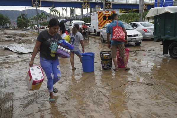 Personas con productos y alimentos sacados de una tienda tras el devastador paso del huracán Otis por Acapulco, México, el miércoles 25 de octubre de 2023. El huracán Otis provocó grandes destrozos al atravesar la costa sur del Pacífico mexicano con categoría 5, al llegar con grandes inundaciones, quebrar carreteras y dejar sin servicio eléctrico y telefónico a grandes partes del estado de Guerrero. (AP Foto/Marco Ugarte)