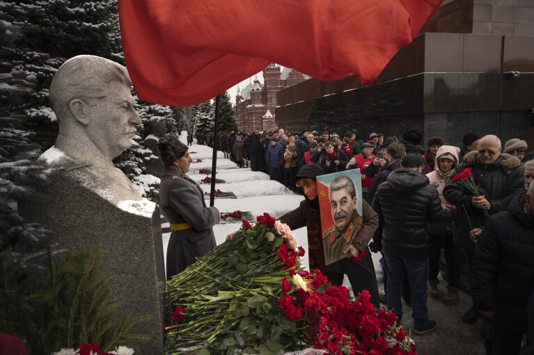 FILE - Communist party supporters with red flags and a portrait of Josef Stalin lineup to place flowers at his grave near the Kremlin Wall to mark the 70th anniversary of his death in Red Square in Moscow, Russia, Sunday, March 5, 2023. Josef Stalin led the Soviet Union from 1924 until his death in 1953. In Russia, history has long become a propaganda tool used to advance the Kremlin's political goals. In an effort to rally people around the flag, the authorities have sought to magnify the country's past victories while glossing over the more sordid chapters of its history. (AP Photo/Alexander Zemlianichenko, File)