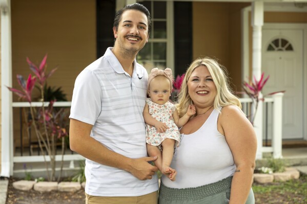Sam Earle, left, poses with his wife, Tori, and their daughter, Novalie, outside their home Tuesday, May 7, 2024, in Lakeland, Fla. Novalie was born through an embryo adoption. Tori views pregnancy with a donated embryo as nurturing “what was already established,” she says. (AP Photo/Mike Carlson)