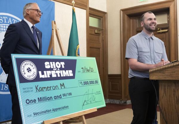 Kameron M., 23, from South King County smiles at a news conference in Olympia, Wash., Friday, July 16, 2021, with Washington Gov. Jay Inslee, left, after accepting a mock check for $1 million, which he won as part of a "Shot of a Lifetime" lottery open to all who got the COVID-19 vaccine. The motorcycle mechanic didn't know about the lottery but said he got his vaccine as soon as he could because he thought it was the right thing to do. Washington is among several states that created lotteries in hopes of increasing the pace of vaccination. (Ellen M. Banner/The Seattle Times via AP)