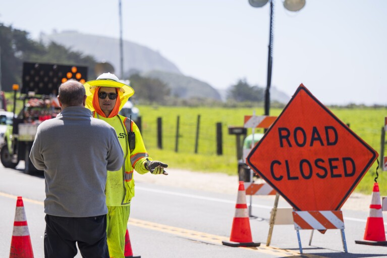 Alejandro Garcia, right, a traffic control technician with Stateside, talks to a tourist at a road closure on Highway 1 near Big Sur, Calif., Monday, April 1, 2024, following an Easter weekend storm. (AP Photo/Nic Coury)