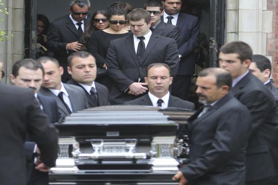 FILE - In this May 22, 2013, file photo, Andrea Rebello's father Fernando, left, twin sister Jessica, second from left and mother Nella, third from left, follow Rebello’s casket after her funeral service at St. Teresa of Avila Church in Sleepy Hollow, N.Y. A Long Island district attorney has decided not to prosecute a police officer who killed the Hofstra University student and the armed intruder who was holding her hostage. Nassau County District Attorney Kathleen Rice issued a 28-page report Wednesday, April 2, 2014, stating that a prosecution of Police Officer Nikolas Budlimic is not warranted. Budlimic fired at the intruder who was holding Rebello in a headlock when he was the first officer to arrive at the report of a home invasion in 2013. One round missed the intruder but struck and killed Rebello by mistake. (AP Photo/Mary Altaffer, File)