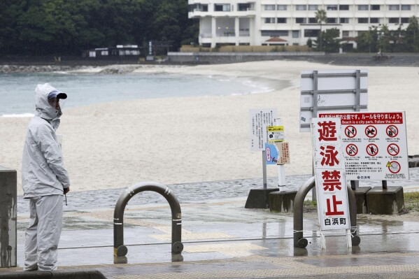 A person stands near a swimming beach in Shirahama, Wakayama prefecture, western Japan Monday, Aug. 14, 2023. Swimming at the beach is banned due to approaching Typhoon Lan. The powerful typhoon was approaching Japan's main archipelago of Honshu on Monday threatening to hit large areas of western and central Japan with heavy rain and high winds, as many people were traveling for a Buddhist holiday week. A notice, foreground, reads " No swimming." (Kyodo News via AP)