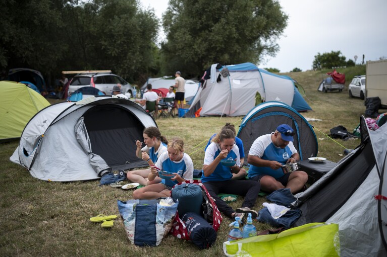 Volunteers have a dinner after a hard working day in their camp near Tiszaroff, Hungary, Tuesday, Aug. 1, 2023. (AP Photo/Denes Erdos)