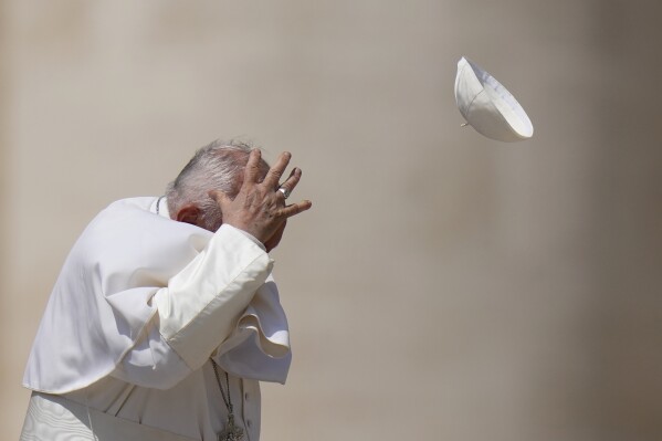Pope Francis tries to catch his cap as wind blew it away while leaving after his weekly general audience in St. Peter's Square at The Vatican, Wednesday, May 15, 2024. (AP Photo/Alessandra Tarantino)
