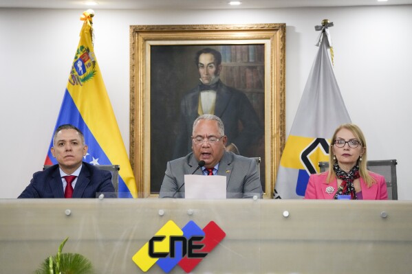 National Electoral Council (CNE) President Elvis Hidrobo Amoroso, center, speaks to the press at the National Electoral Council headquarters, flanked by Carlos Enrique Quintero, left, and Rosalba Gil in Caracas, Venezuela, Tuesday, March 5, 2024. Amoroso announced that Venezuela's presidential election will take place on July 28. Behind is a portrait of independence hero Simon Bolivar. (AP Photo/Ariana Cubillos)
