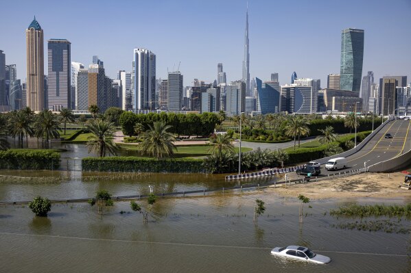 An abandoned vehicle stands in floodwater caused by heavy rain with the Burj Khalifa, the world's tallest building, seen on the background, in Dubai, United Arab Emirates, Thursday, April 18, 2024. The United Arab Emirates attempted to dry out Thursday from the heaviest rain the desert nation has ever recorded, a deluge that flooded out Dubai International Airport and disrupted flights through the world's busiest airfield for international travel. (AP Photo/Christopher Pike)