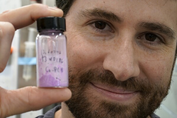 Jarad Mason, assistant professor of chemistry and chemical biology at Harvard University, of Watertown, Mass., holds a vile of cobalt-based hybrid material, Thursday, Sept. 14, 2023, in a lab on the school's campus, in Cambridge, Mass. The material is part of research to develop a more environmentally-friendly solid refrigerant that could be used as an alternative to existing volatile refrigerants. (AP Photo/Steven Senne)