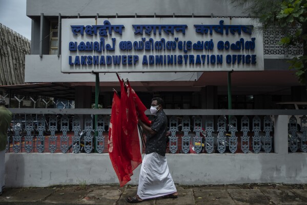 FILE- An activist of Centre of Indian Trade Unions (CITU) walks with flags after a protest outside the Lakshadweep administration office in Kochi, Kerala state, India, June 15, 2021. India announced plans for a new naval base off the country’s south-west coast and close to Maldives, as tensions are running high between Delhi and the island nation. The Indian Navy said Saturday it plans to build a base called INS Jatayu on Minicoy, the southernmost island in the Lakshadweep archipelago. (AP Photo/R S Iyer, File)