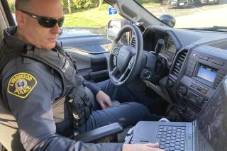 FILE - Lynnwood police Officer Denis Molloy works in his vehicle, Wednesday, Nov. 17, 2021, in Lynnwood, Wash. Molloy is part of the Lynnwood Police Department's community health and safety section. Washington Gov. Jay Inslee has signed two bills fixing parts of a sweeping package of police reform measures that lawmakers passed last year. One makes clear officers may use force to help detain or transport people in behavioral health crisis, while the other fixes an oversight that seemed to inadvertently prohibit police departments from possessing certain less-lethal weapons. (AP Photo/Gene Johnson,File)