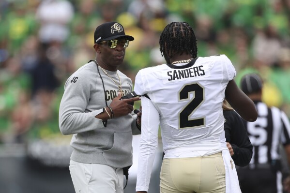 Colorado head coach Deion Sanders talks with his son and quarterback Shedeur Sanders during the first half of an NCAA college football game against Oregon, Saturday, Sept. 23, 2023, in Eugene, Ore. (AP Photo/Amanda Loman)