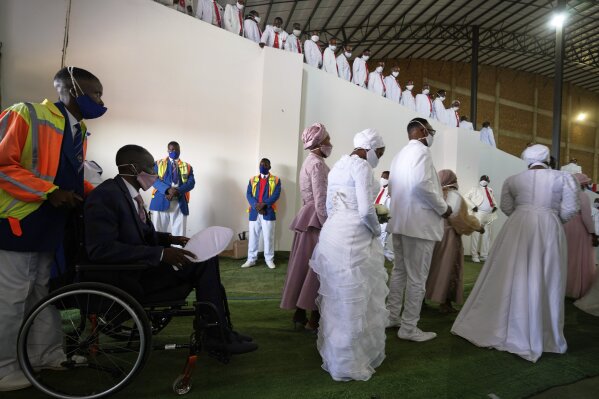 A groom in a wheelchair is assisted by a fellow member whilst his two brides walk in front, during mass Easter weddings for 3,000 people, some polygamous, at The International Pentecost Holiness Church in Heidelberg, east of Johannesburg, South Africa, Sunday, April 20, 2025. (AP Photo/Themba Hadebe)
