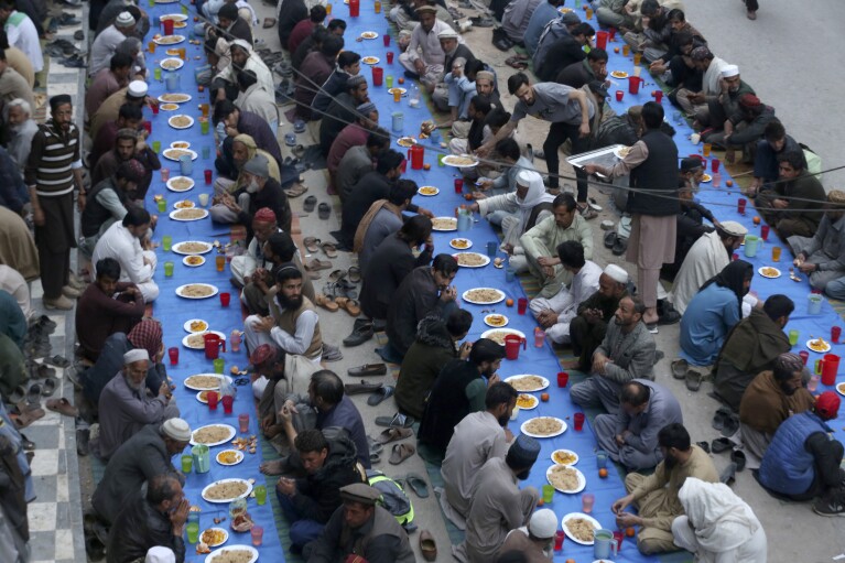 People wait to break their fast during the Muslim's holy fasting month of Ramadan, at a free meal distribution point in Peshawar, Pakistan, Tuesday, March 12, 2024. (AP Photo/Muhammad Sajjad)