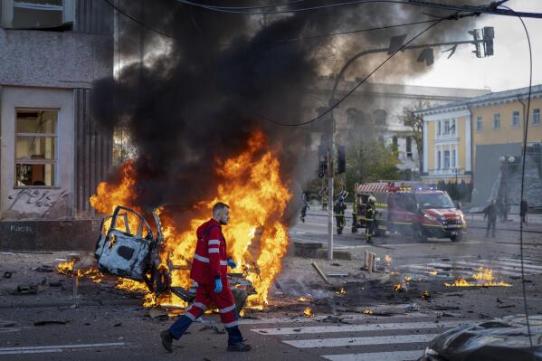 A medical worker runs past a burning car after a Russian attack in Kyiv, Ukraine, Monday, Oct. 10, 2022. The Russian missiles that rained down Monday on cities across Ukraine, bringing fear and destruction to areas that had seen months of relative calm, are an escalation in Moscow's war against its neighbor. But military analysts say it’s far from clear whether the strikes mark a turning point in a war that has killed thousands of Ukrainians and sent millions fleeing from their homes. (AP Photo/Roman Hrytsyna)