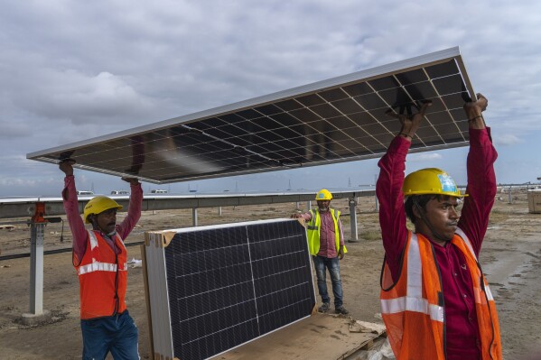 Workers carry a solar panel for installation at the under-construction Adani Green Energy Limited's Renewable Energy Park in the salt desert of Karim Shahi village, near Khavda, Bhuj district near the India-Pakistan border in the western state of Gujarat, India, Thursday, Sept. 21, 2023. India is developing a 30 gigawatt hybrid — wind and solar — renewable energy project on one of the largest salt deserts in the world. (AP Photo/Rafiq Maqbool)