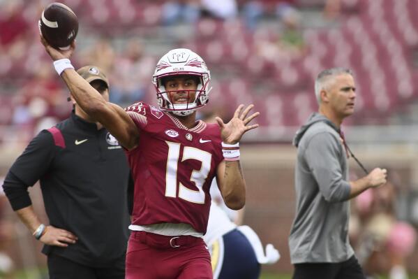 Florida State quarterback Jordan Travis (13) warms up as Florida State head coach Mike Norvell walks past him before an NCAA college football game against Georgia Tech, Saturday, Oct. 29, 2022, in Tallahassee, Fla. (AP Photo/Phil Sears)