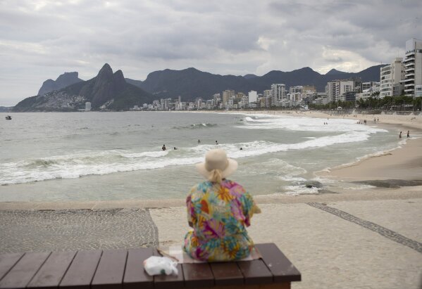 An elderly woman watches Arpoador beach in Rio de Janeiro, Brazil, Tuesday, March 17, 2020. Firemen began blaring recordings that urge beachgoers to stay home on Monday, one day before Rio's Gov. Wilson Witzel decreed a state of emergency. For most people, the new coronavirus causes only mild or moderate symptoms, such as fever and cough. For some, especially older adults and people with existing health problems, it can cause more severe illness, including pneumonia. (AP Photo/Silvia Izquierdo)