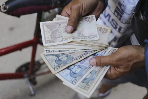 An ice cream street vendor shows his Cuban pesos in Havana, Cuba, Monday, April 20, 2024. An increasing number of Cubans are having to grapple with the country's shortage of cash. Converting those Cuban pesos to other currencies poses yet another challenge, as there are several, highly fluctuating exchange rates in the island. (AP Photo/Ariel Ley)