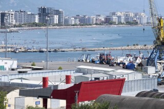 FILE - People gather on the beach as a migrant center is seen in the foreground in the port of Shengjin, northwest Albania, July 25, 2024. (AP Photo/Vlasov Sulaj, File)
