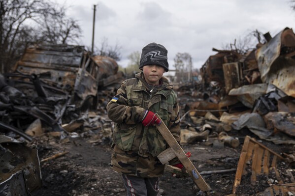 Yehor, 7, stands holding a wooden toy rifle next to destroyed Russian military vehicles near Chernihiv, Ukraine, Sunday, April 17, 2022. (AP Photo/Evgeniy Maloletka)