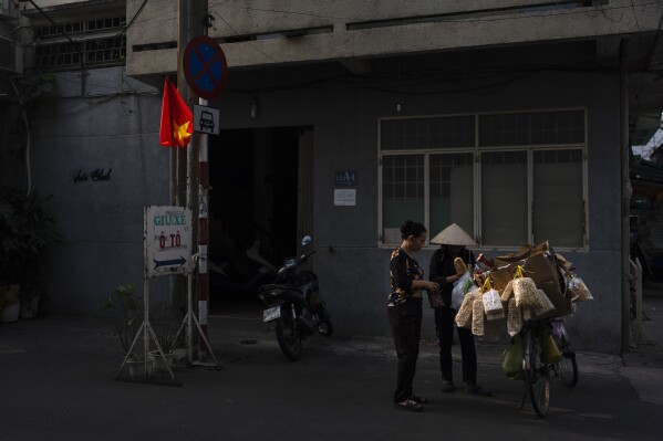 A woman buys bread from a street vendor as a Vietnamese flag is lit by morning sunlight in Ho Chi Minh City, Vietnam, Jan. 11, 2024. (AP Photo/Jae C. Hong)