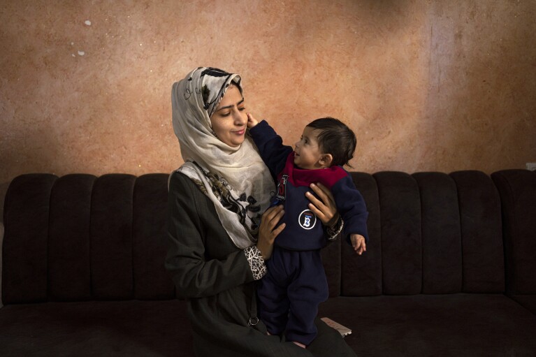 CORRECTS LOCATION - Amal Al-Taweel plays with her baby Ali at her family home in Nuseirat, central Gaza Strip, Friday, April 5, 2024. Ali was born Oct. 7, the day the Israel-Hamas war erupted. Mothers who gave birth in the Gaza Strip that day fret that their 6-month-old babies have known nothing but brutal war, characterized by a lack of baby food, unsanitary shelter conditions and the crashing of airstrikes. (AP Photo/Fatima Shbair)