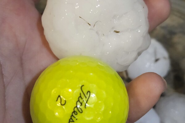 In this image provided by Randy Smith, a large chunk of hail is compared to the size of a golf ball, Wednesday night, March 13, 2024, in Shawnee, Kan. Volatile weather was honing in on parts of Kansas and Missouri Wednesday night, with some storms bringing massive chunks of hail. (Randy Smith via AP)