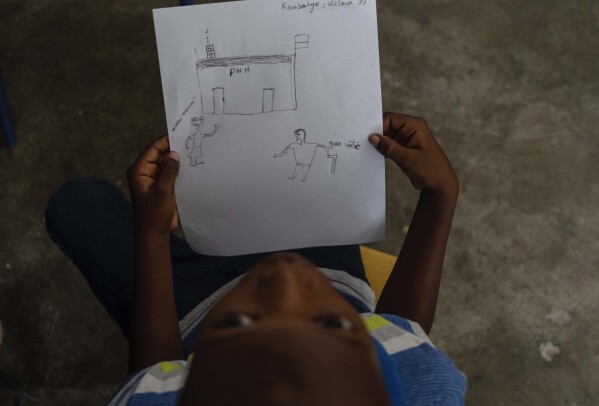 Jadlenzky Louis sostiene un dibujo realizado por su madre Guirlaine Reveil que muestra a un hombre empuñando un arma mientras se acerca a una comisaría, un escenario de la vida real ocurrido hace un par de años, durante una clase para adultos para aprender a ayudar a sus hijos. superar el trauma y el miedo en medio de la violencia, en Puerto Príncipe, Haití, el domingo 5 de mayo de 2024. A medida que los jóvenes haitianos están cada vez más expuestos a la violencia, el país está realizando un esfuerzo más amplio para disipar un tabú de larga data sobre la búsqueda de terapia y hablando de salud mental. (Foto AP/Ramón Espinosa)