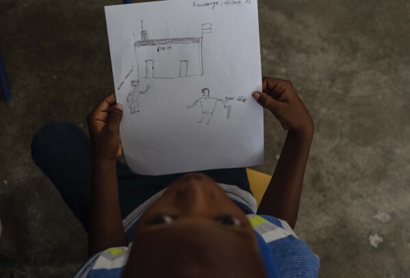 Jadlenzky Louis holds a drawing made by his mother Guirlaine Reveil that shows a man holding a gun as she approaches a police station, a real-life scenario that occurred a couple of years ago, during a class for adults to learn how to help their children overcome trauma and fear amid violence, in Port-au-Prince, Haiti, Sunday, May 5, 2024. As young Haitians are increasingly exposed to violence, the country is undergoing a wider push to dispel a long-standing taboo on seeking therapy and talking about mental health. (AP Photo/Ramon Espinosa)