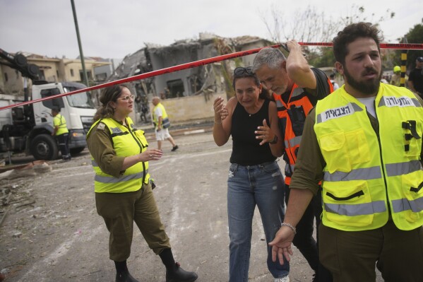 A rescue worker evacuates a woman from the site where a missile launched from Iran struck in Nes Ziona ,Israel, Sunday, June 22, 2025. (AP Photo/Ohad Zwigenberg)