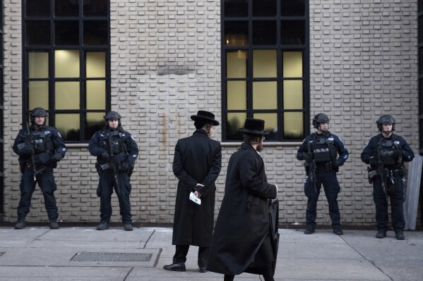 FILE - Orthodox Jewish men pass New York City police guarding a Brooklyn synagogue on Dec. 11, 2019, prior to a funeral for Mosche Deutsch, a rabbinical student from Brooklyn who was killed in a shooting at a Jersey City, N.J., market. Ahead of the High Holidays, encompassing Rosh Hashana and Yom Kippur, that begin this week, a network of Jewish security experts and religious leaders hosted several webinars to help prepare for the season. Over recent years, in the face of increased antisemitic threats and violence, the season also is a time of heightened vigilance. (AP Photo/Mark Lennihan, File)