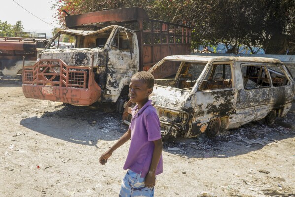 A youth walks by charred cars outside a police station set on fire by armed gangs in Port-au-Prince, Haiti, Tuesday, March 5, 2024. (AP Photo/Odelyn Joseph)